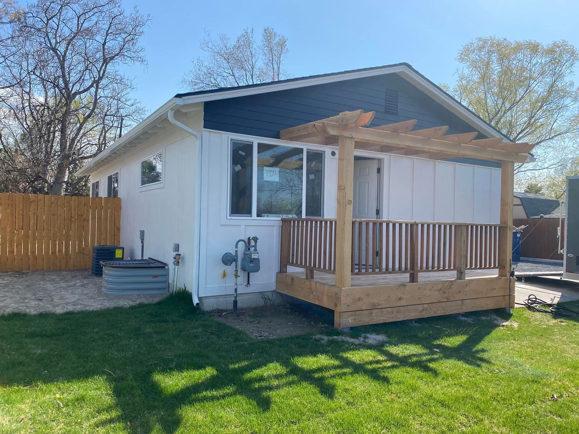 White house with wooden deck, pergola, and brown fence on a green lawn.