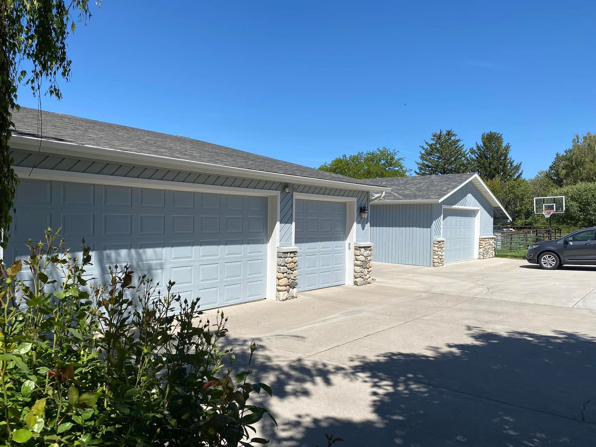 Light blue garage doors with stone accents under a blue sky, car parked in driveway.