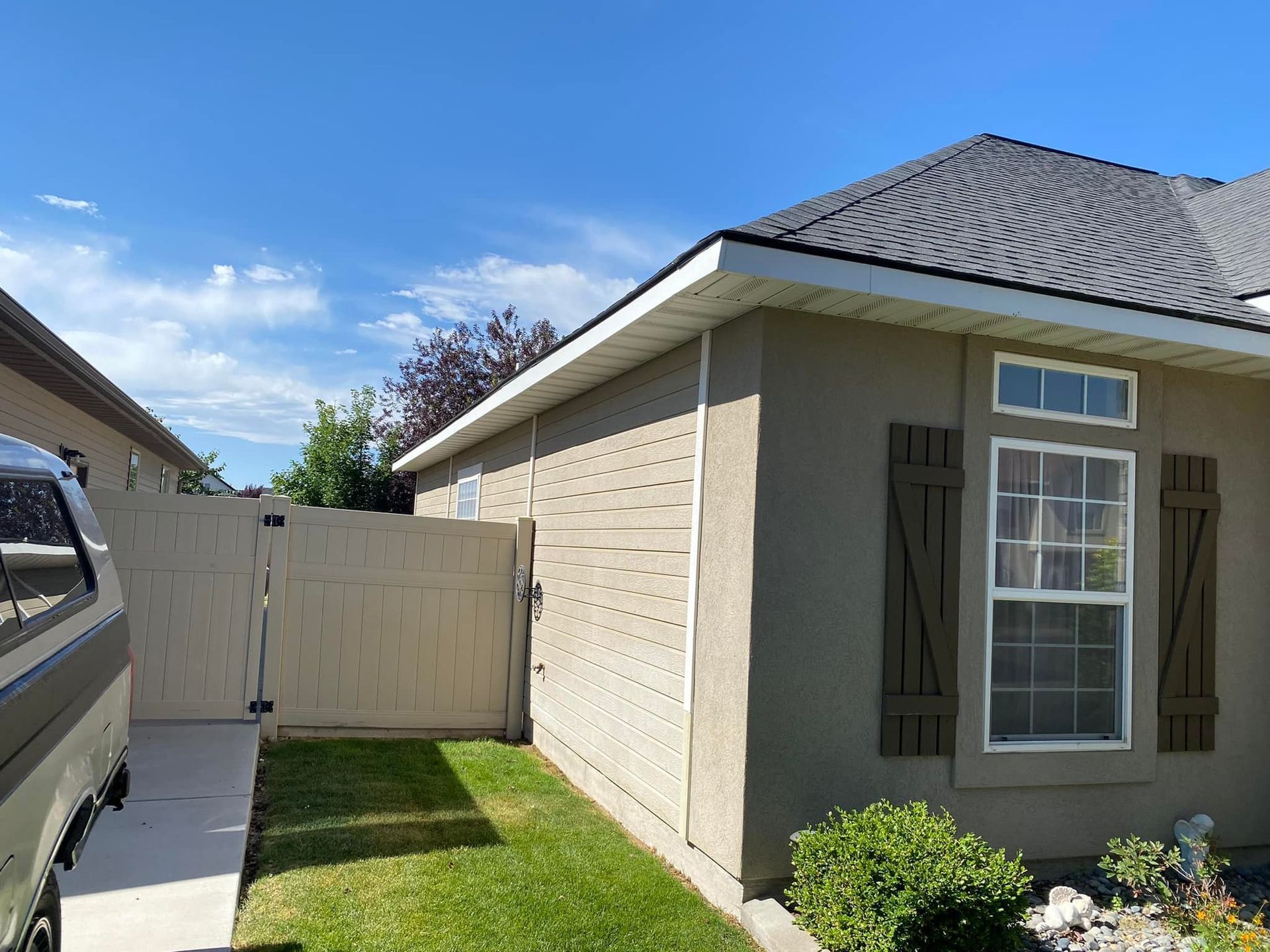 Beige house with a tan fence, green lawn, and blue sky.