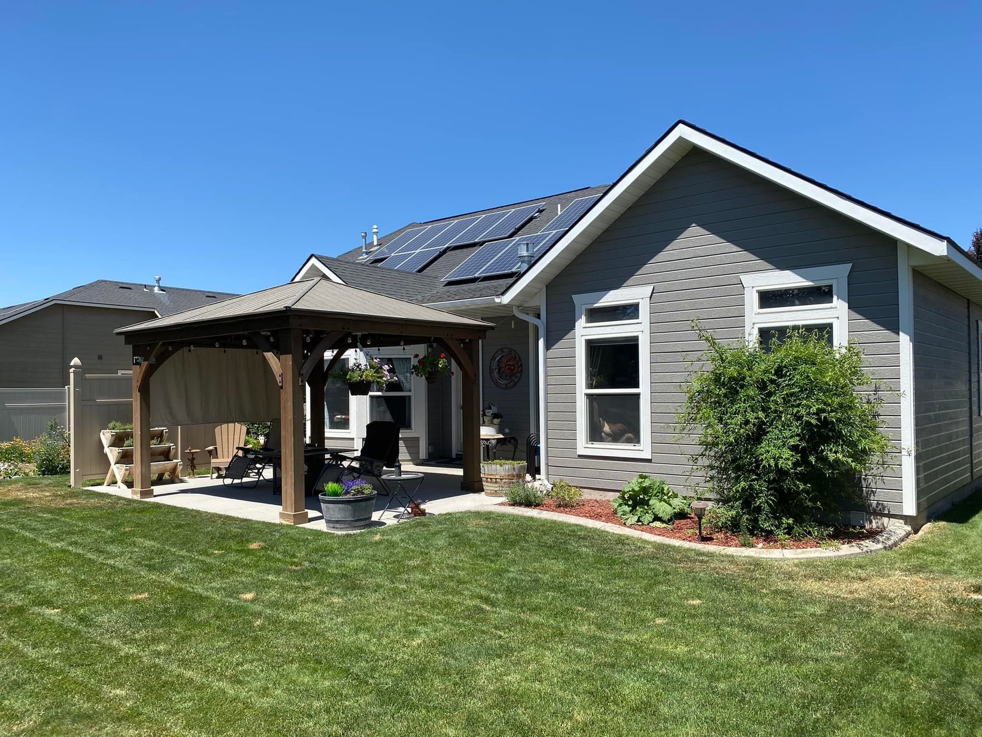 Backyard with gazebo, gray house, solar panels on roof, and green lawn.