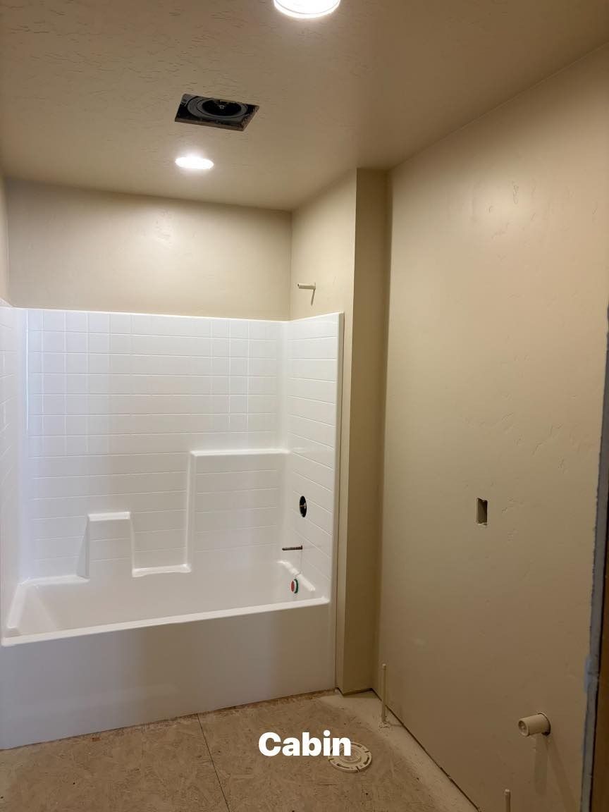 Bathroom with white bathtub and shower surround, beige walls, and a recessed ceiling vent.