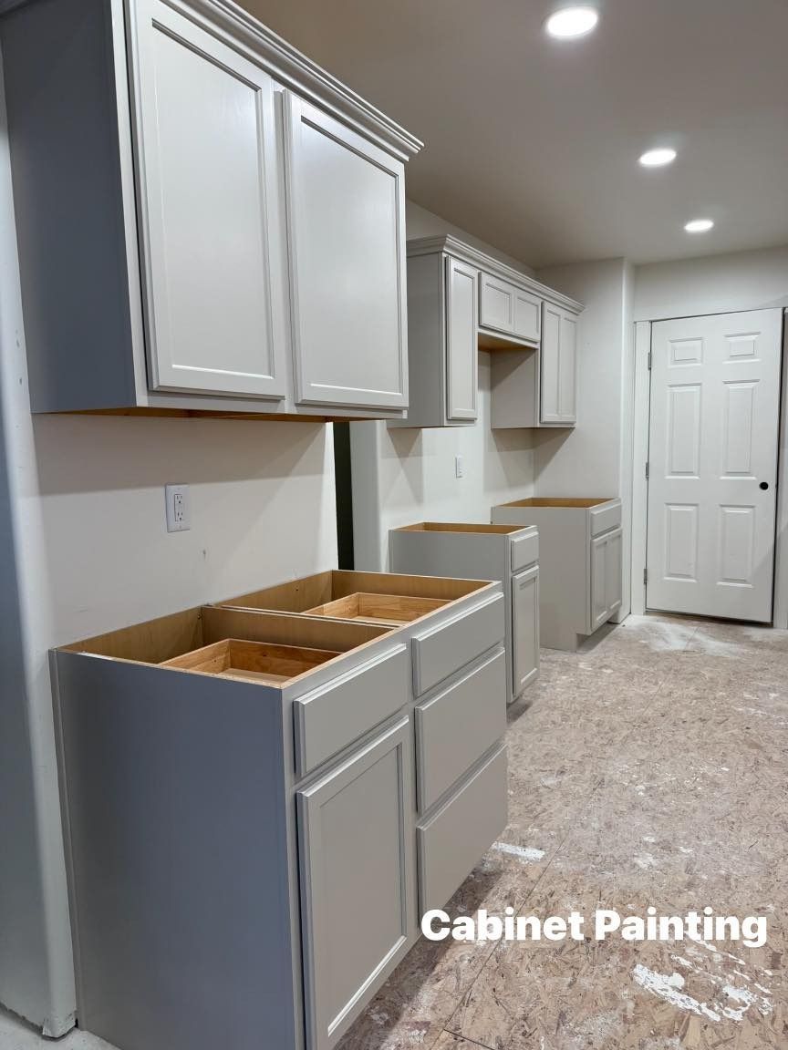 Kitchen cabinets, light gray, installed and awaiting countertops, with a white door and bare floor.