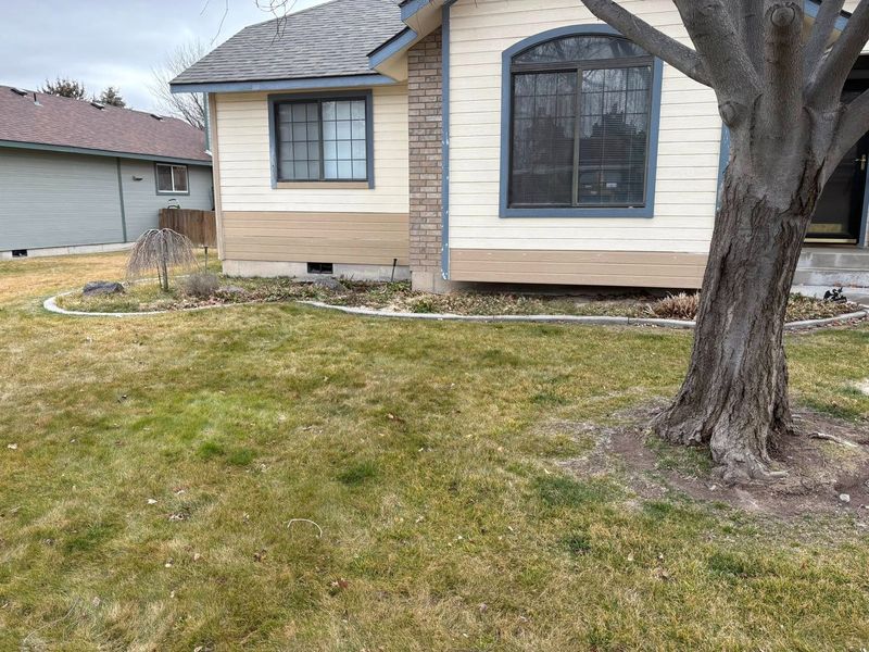 A house with a beige exterior, a gray roof, and a front yard with sparse grass. A tree is to the right.