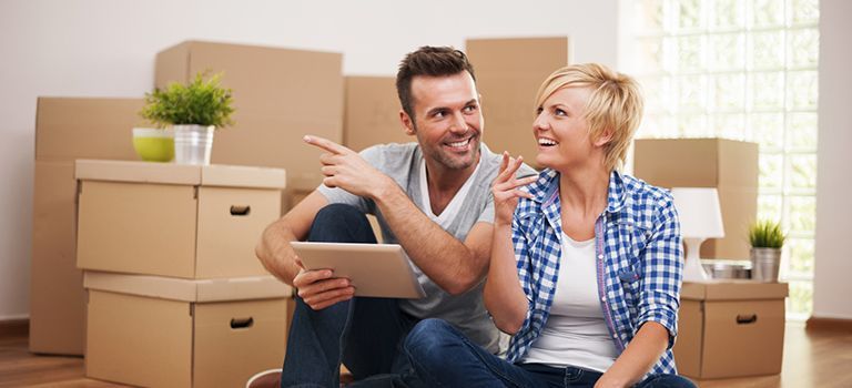 A man and a woman are sitting on the floor looking at a tablet.