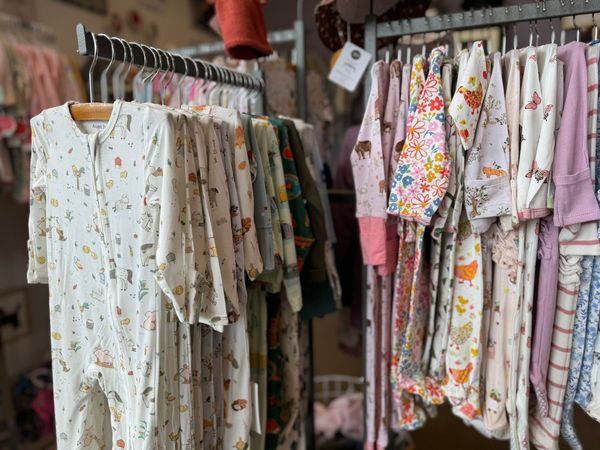 A row of baby clothes hanging on a rack in a store.