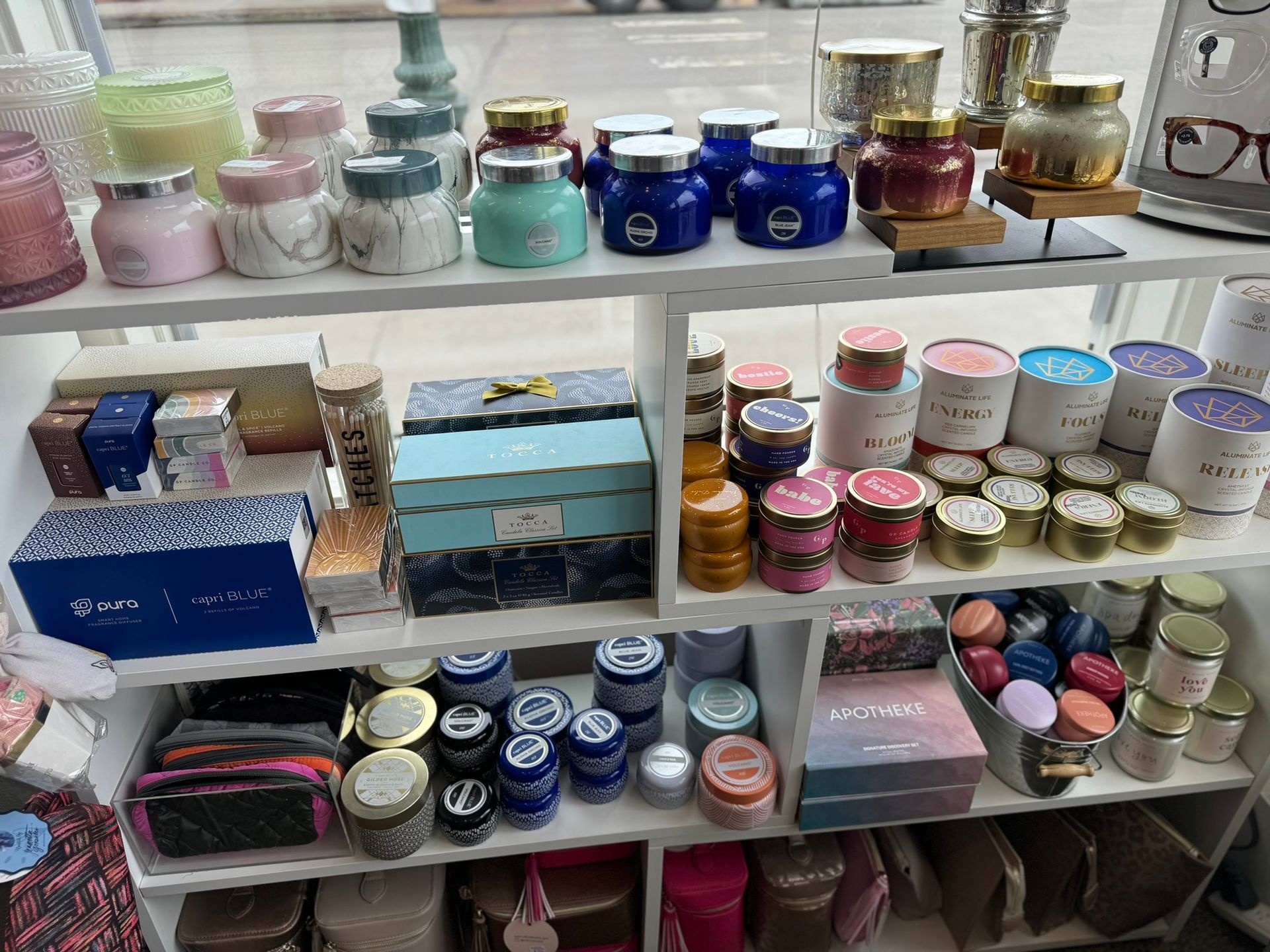 A shelf filled with lots of different types of candles and cosmetics.