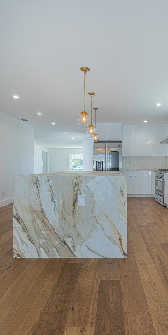 Kitchen with a marble island, wooden floor, and pendant lights.