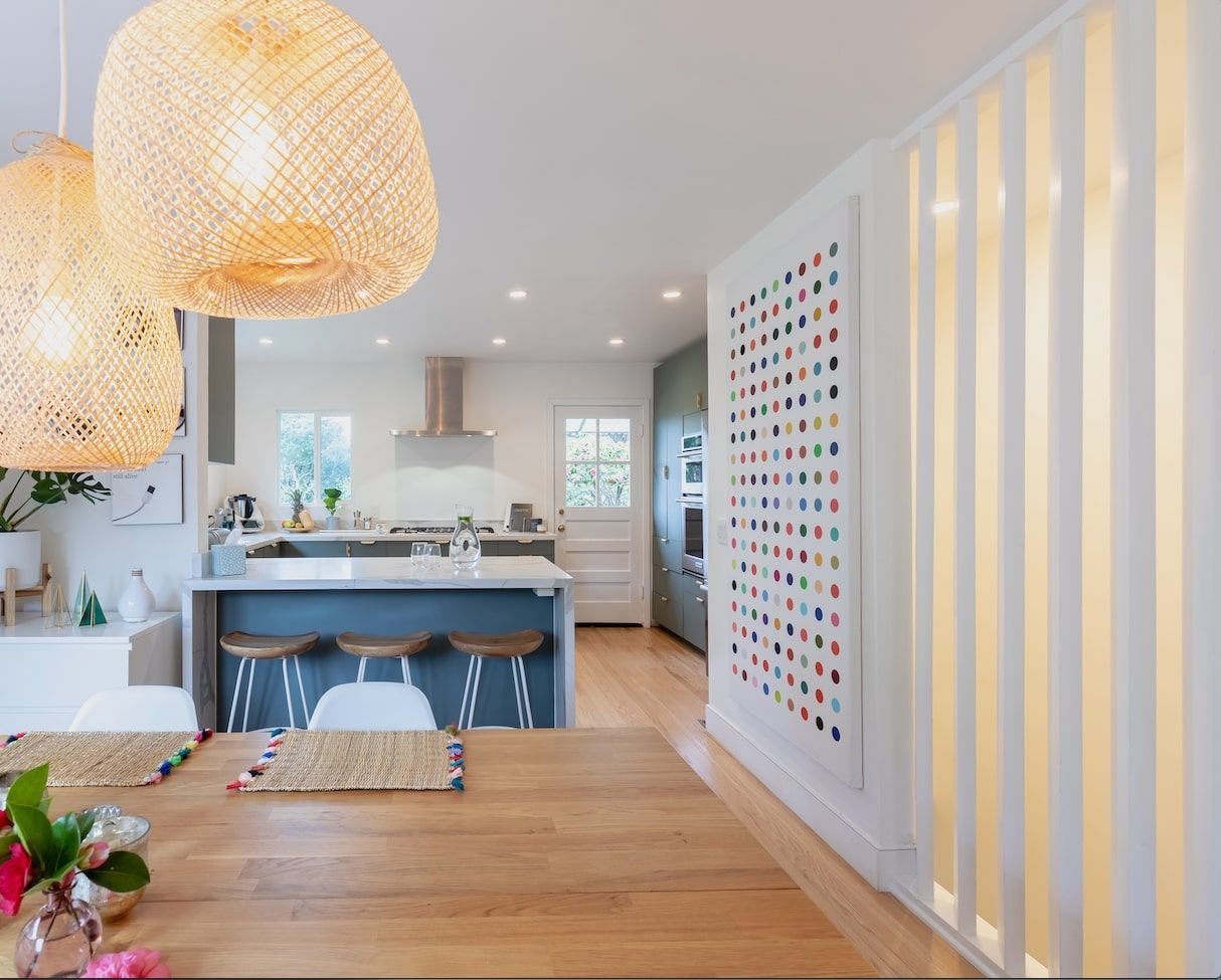 Kitchen with blue island, wooden table, woven pendant lights, and colorful framed art.