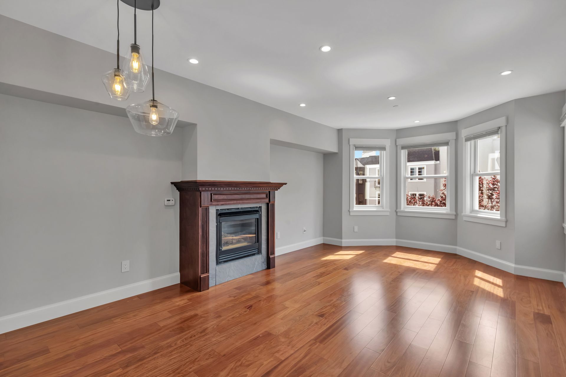 Empty living room with hardwood floors, fireplace, and bay windows.