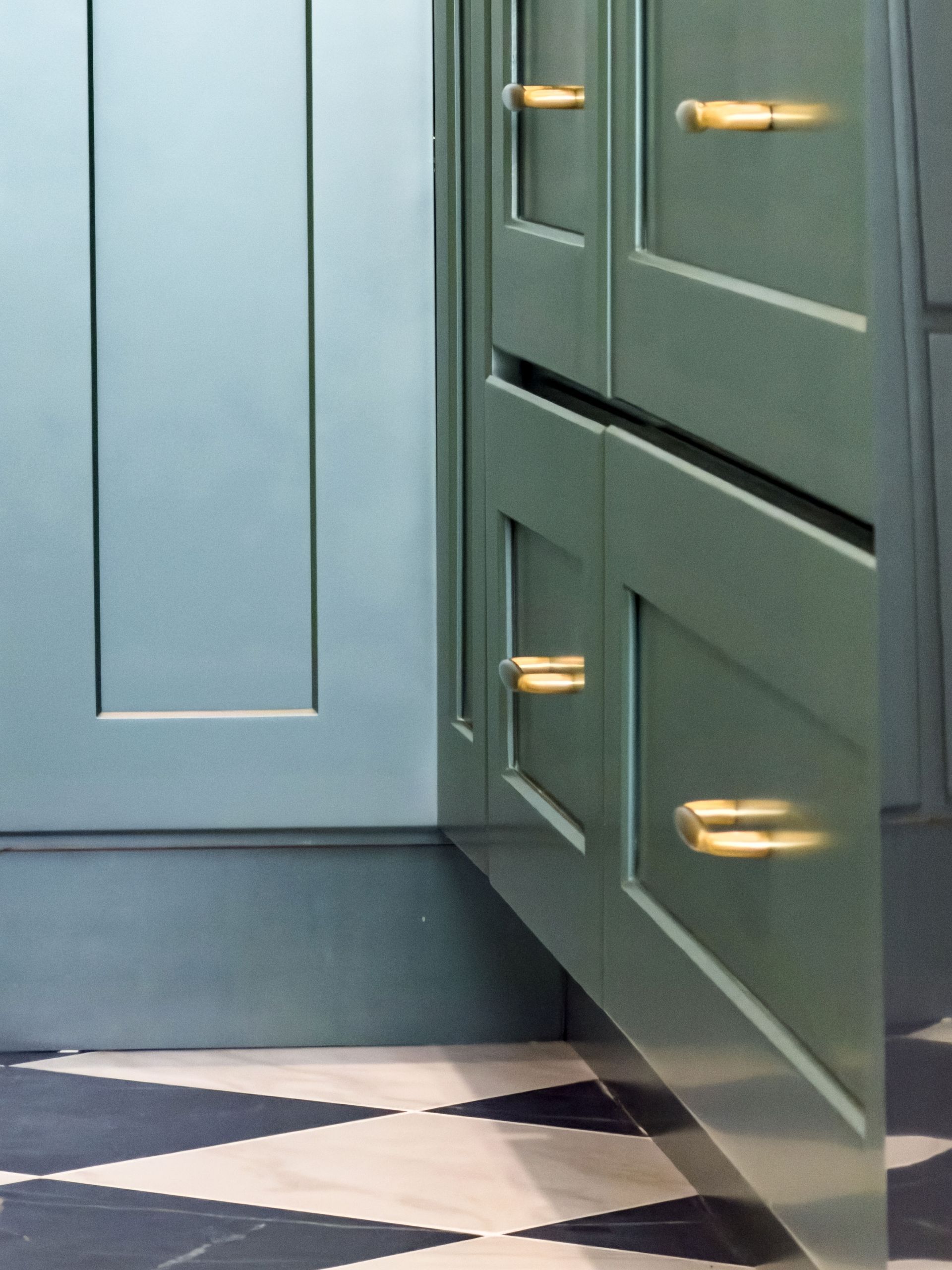 Blue and green cabinets with gold handles, contrasting against a black and white tiled floor.