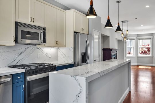 Modern kitchen with white and blue cabinets, stainless steel appliances, and quartz countertops.