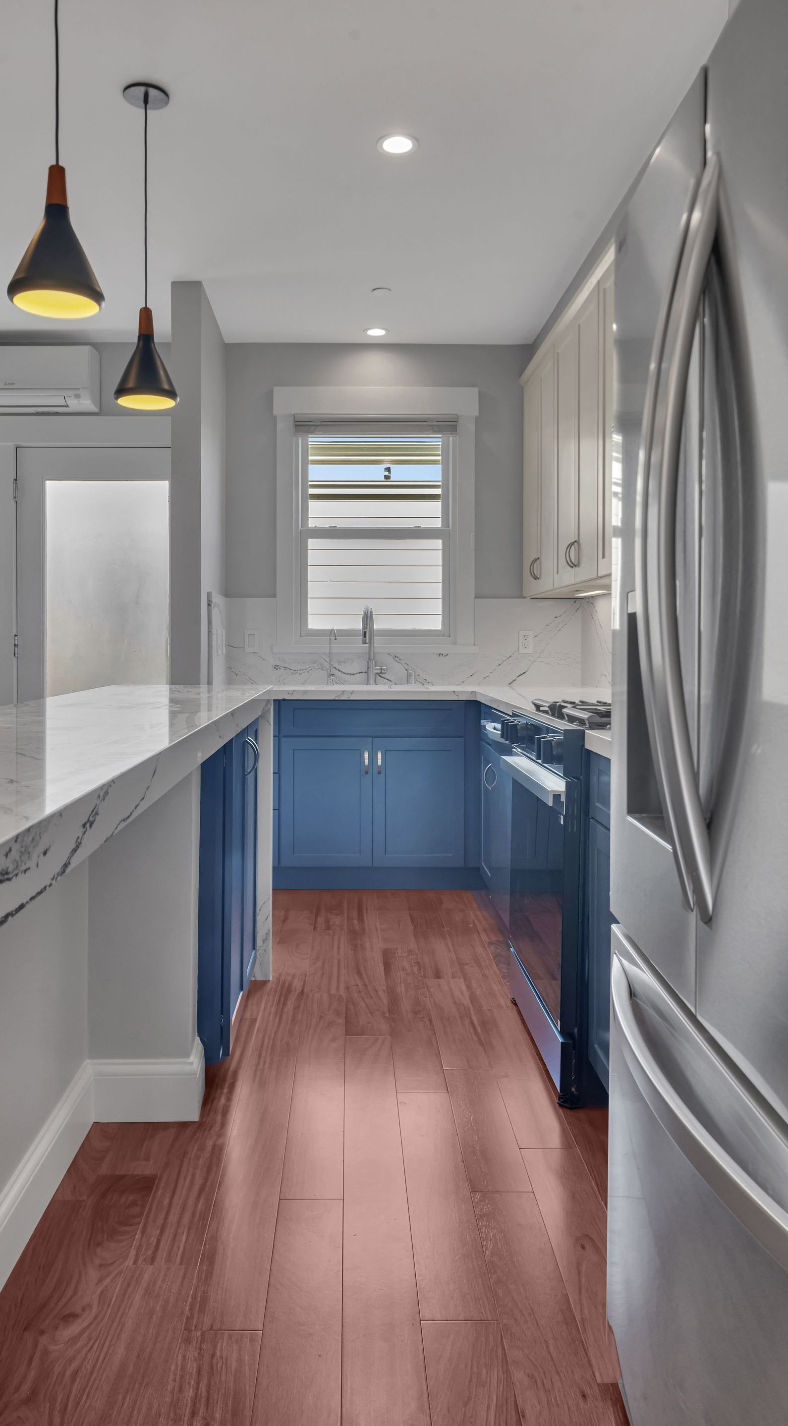 Modern kitchen with blue cabinets, wood floor, stainless steel appliances, and pendant lights.