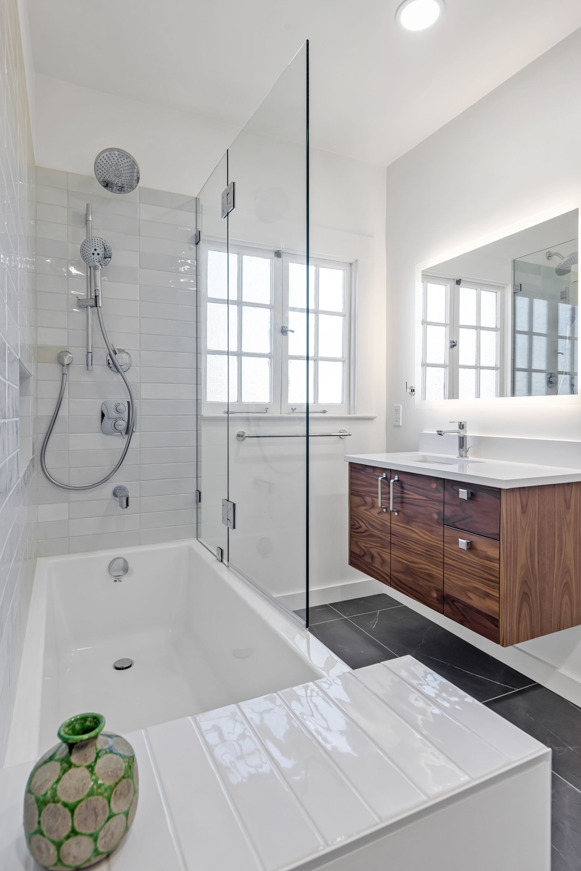 Modern white bathroom with glass shower, wooden vanity, and tub.