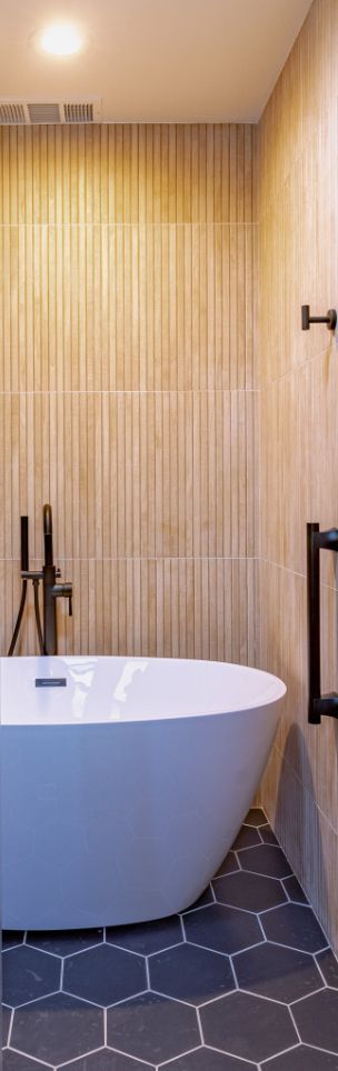 A modern bathroom with a white tub, dark fixtures, and hexagon tile flooring.
