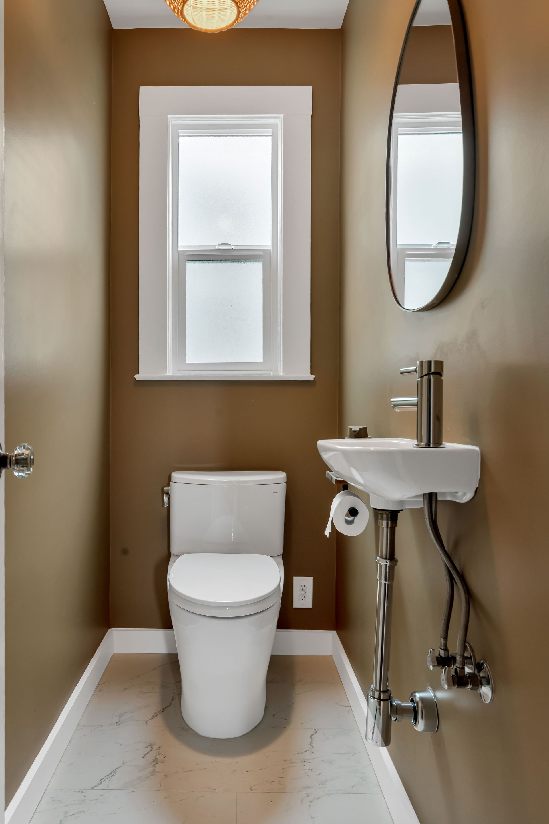 Small bathroom with toilet, sink, and window; brown walls, white trim, and light floor.