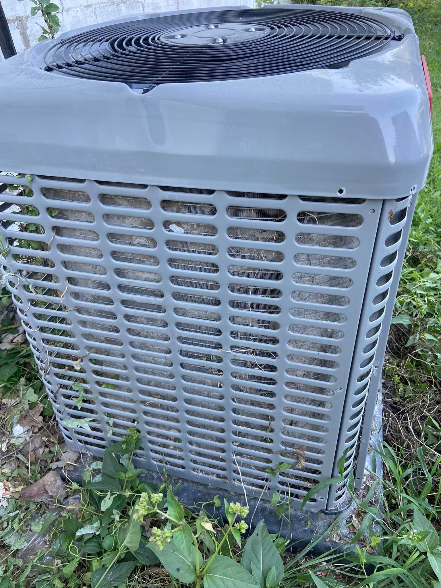 A large gray air conditioner is sitting in the grass.
