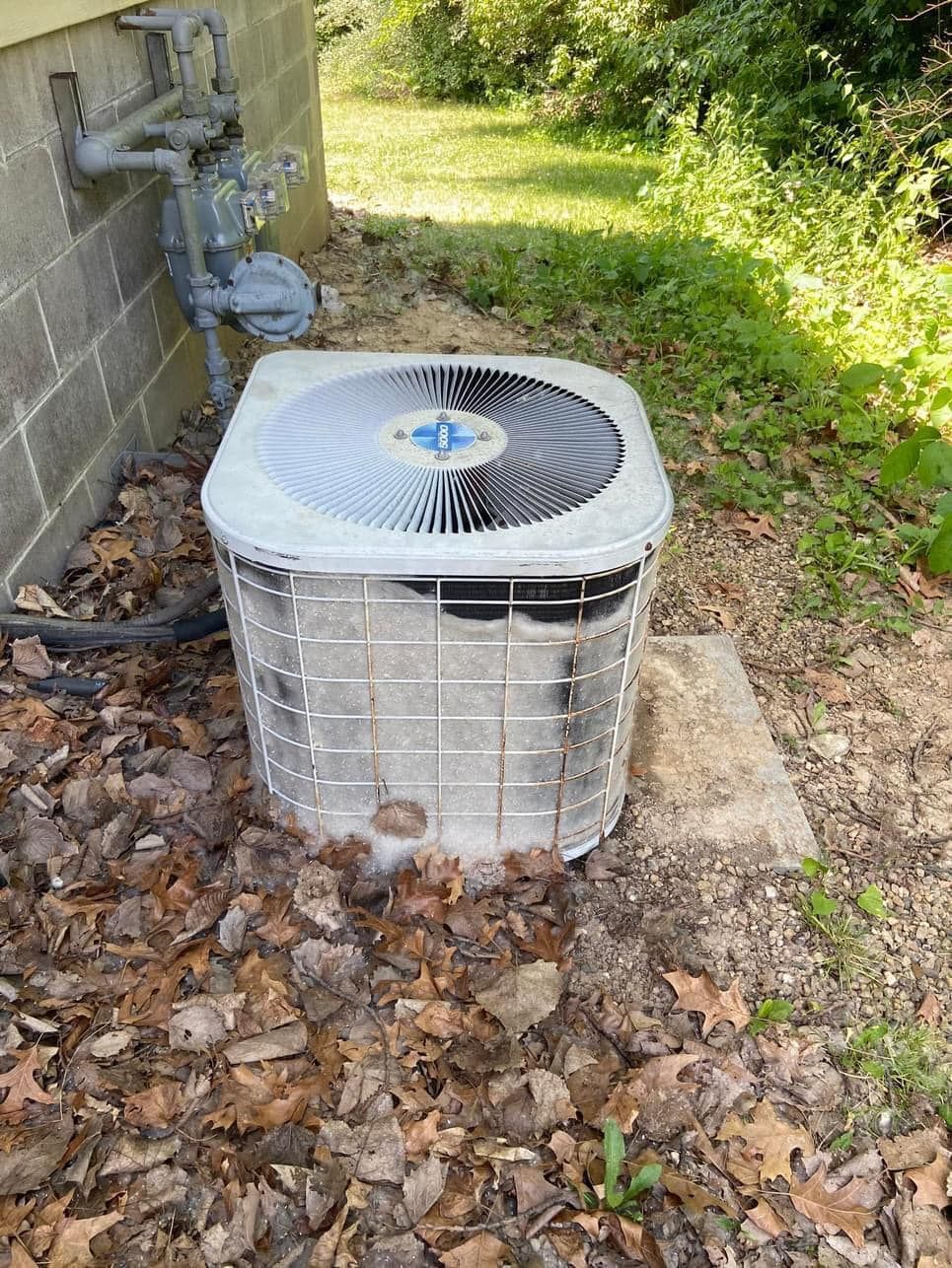 An air conditioner is sitting on the ground next to a brick wall.