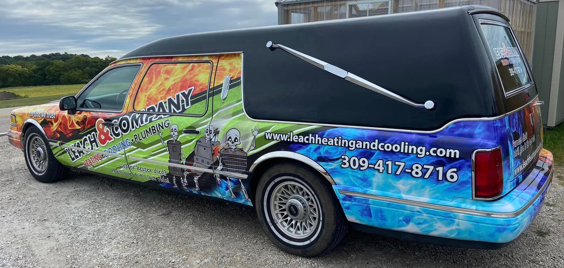 A colorful funeral van is parked on a gravel road.