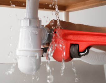 A person is fixing a leaking sink pipe with a wrench.