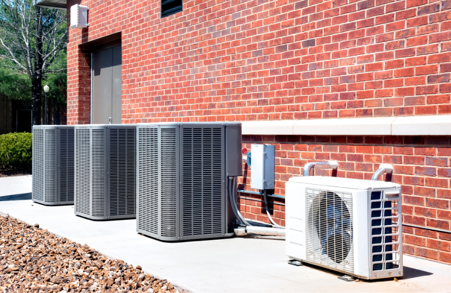 A row of air conditioners are sitting outside of a brick building.