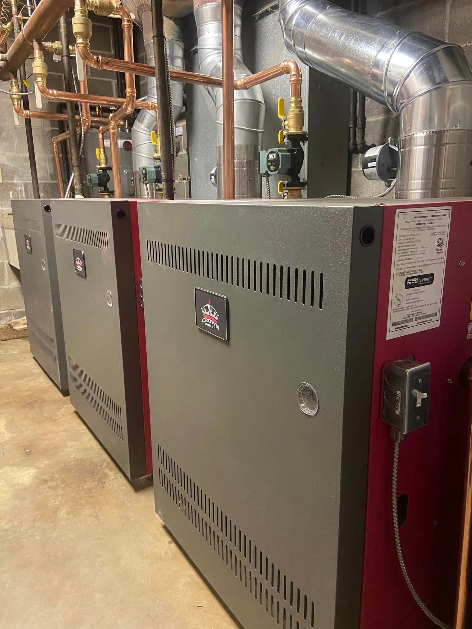 A row of boilers are lined up in a room with pipes.