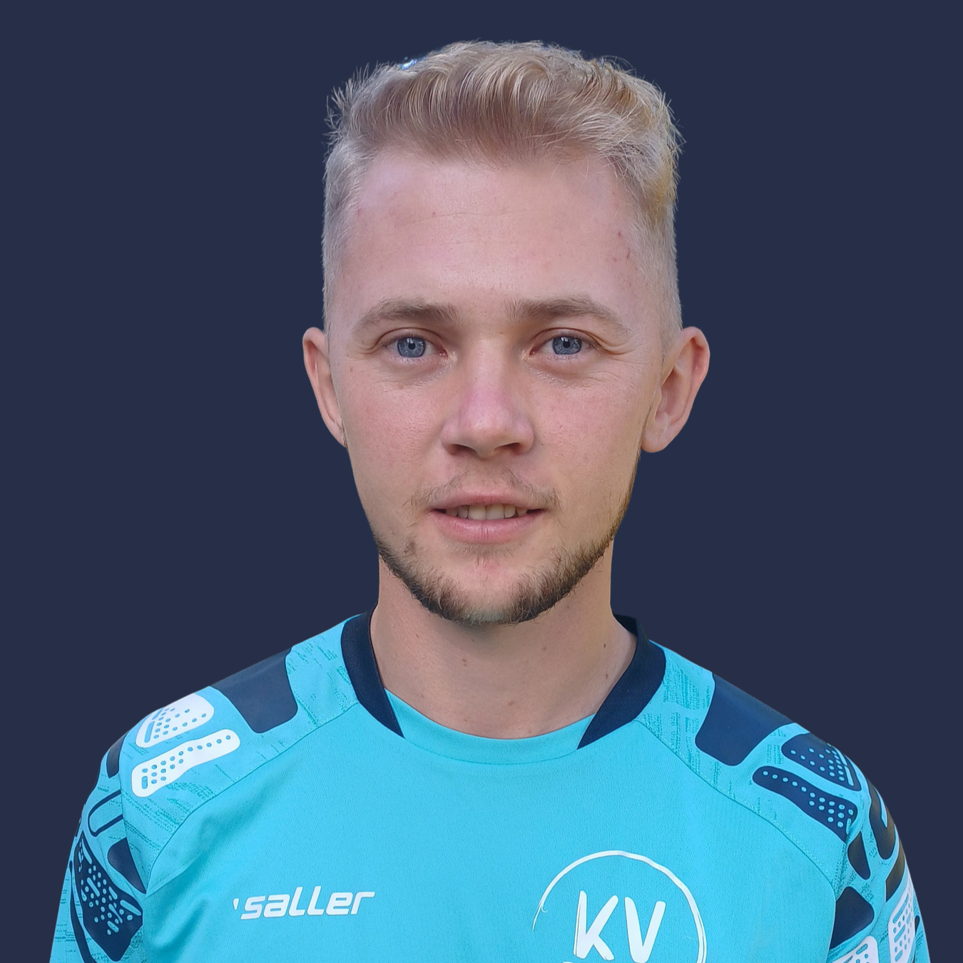 Mladý muž v modročervené pruhované košili stojí se zkříženýma rukama.