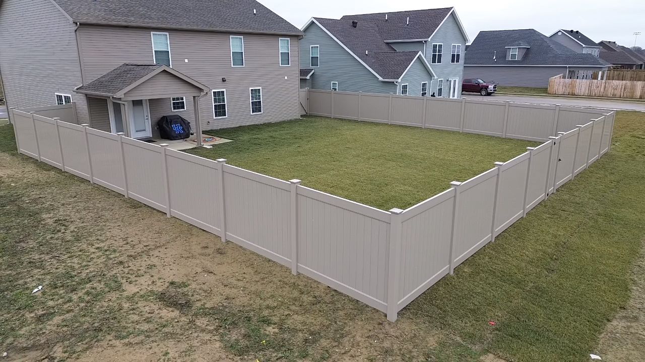 A large fence surrounds a lush green yard in front of a house.