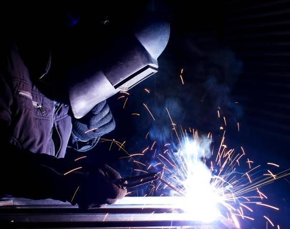 A man wearing a welding mask is welding a piece of metal