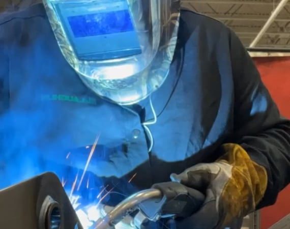 A man wearing a welding helmet is welding a pipe