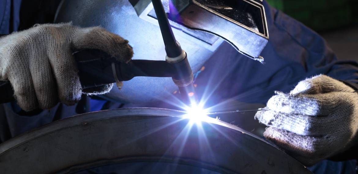A man is welding a piece of metal with a welding machine.