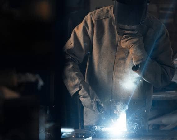 A man is welding a piece of metal in a dark room.