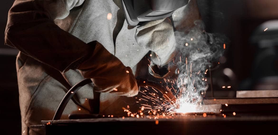 A man is welding a piece of metal in a factory.