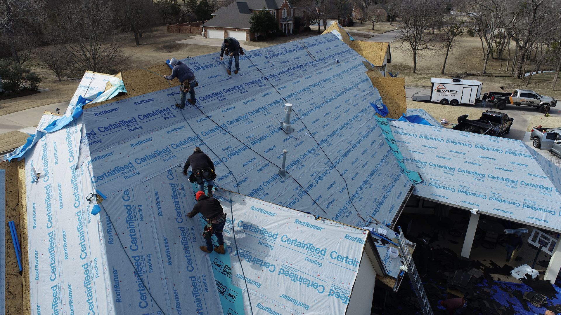 Workers installing blue roofing panels on a house roof during construction or repair.