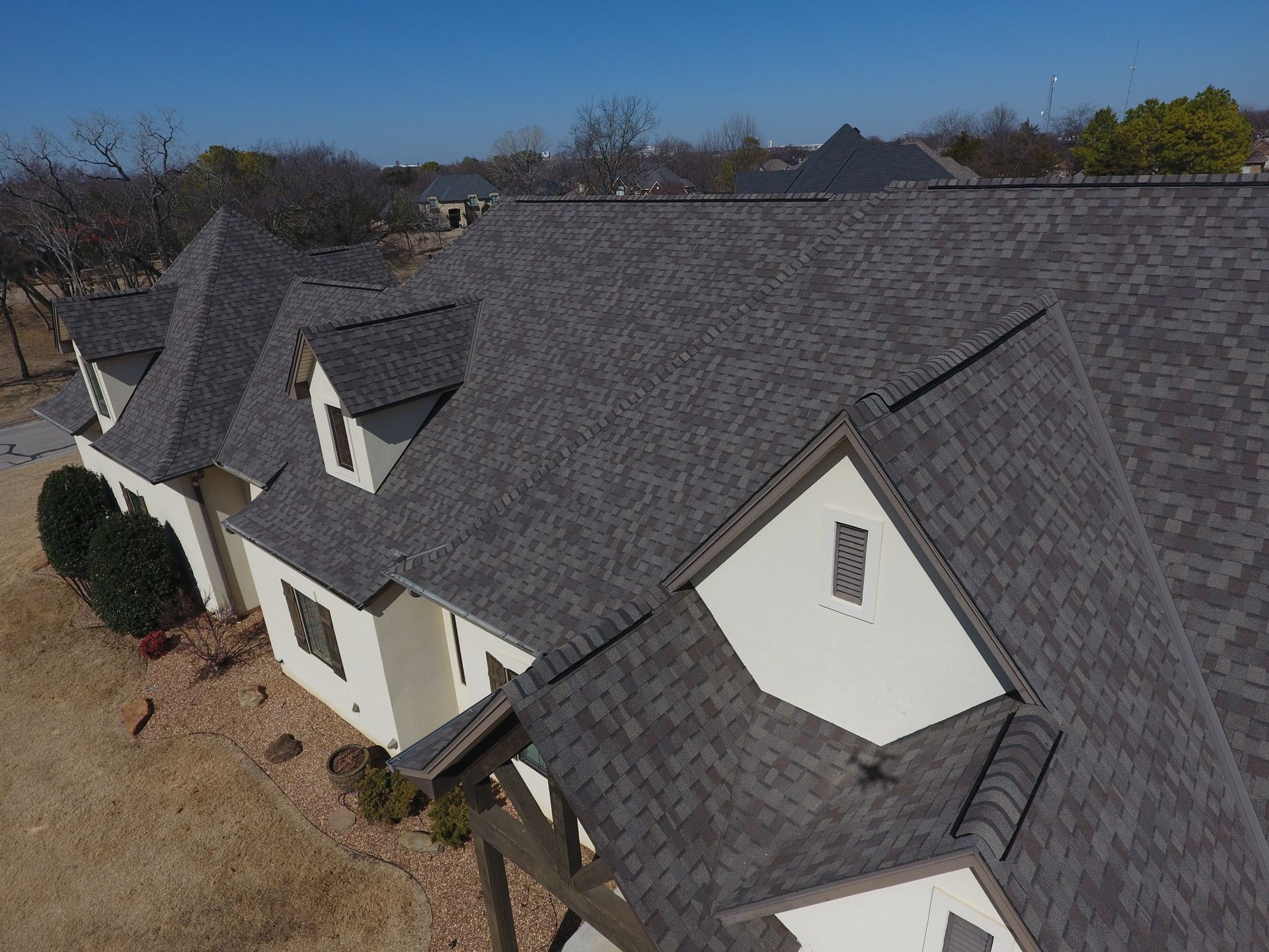 Aerial view of a large gray-shingled house with multiple gables and a beige exterior.