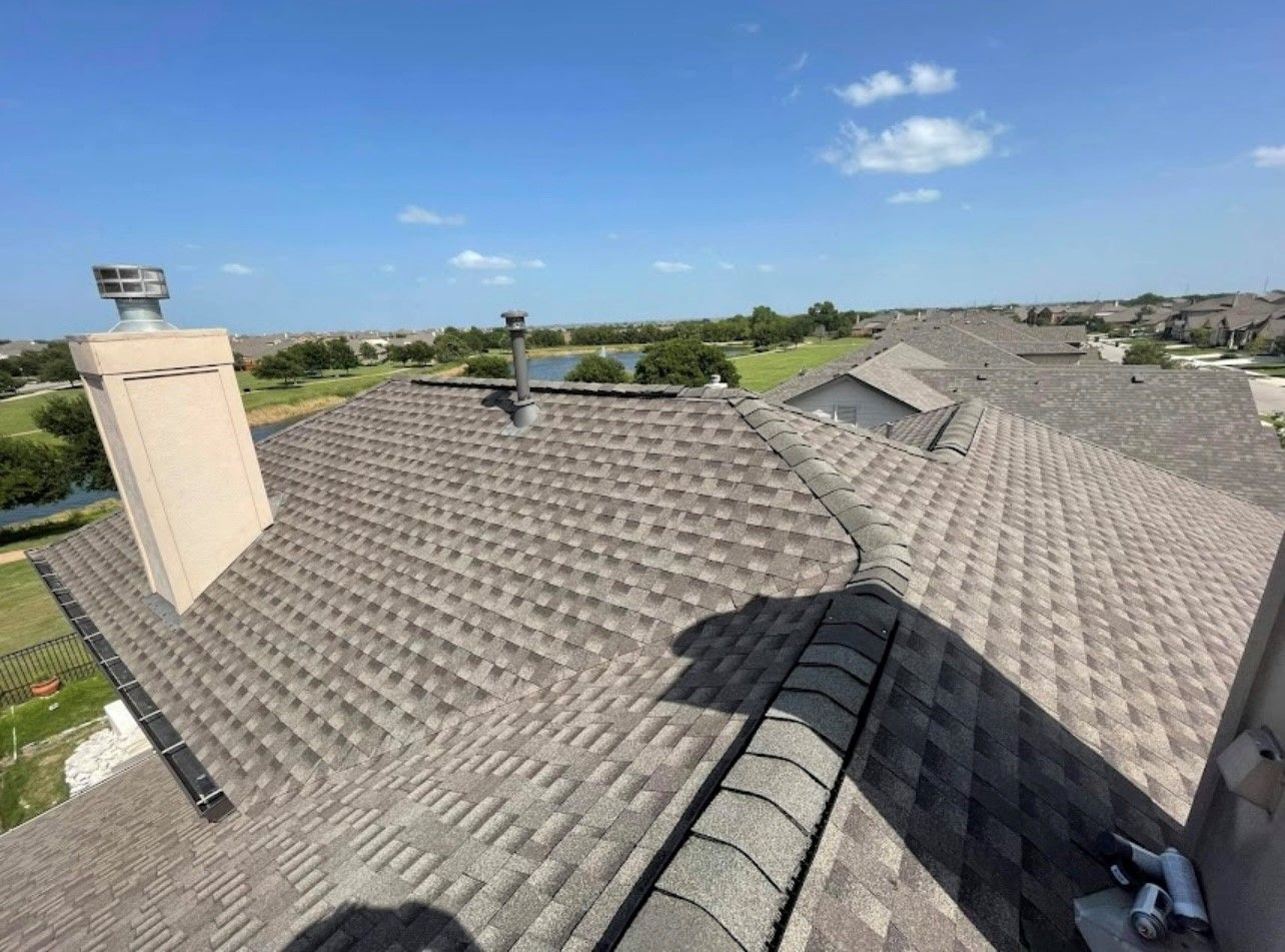 View of shingled roof with chimneys, overlooking neighborhood under blue sky.