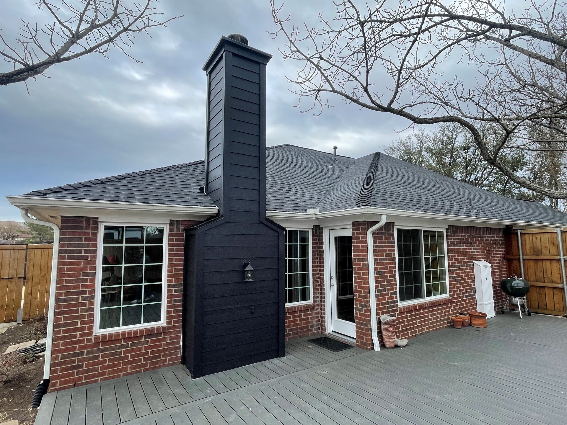 Red brick house with a large black chimney, gray deck, and cloudy sky.