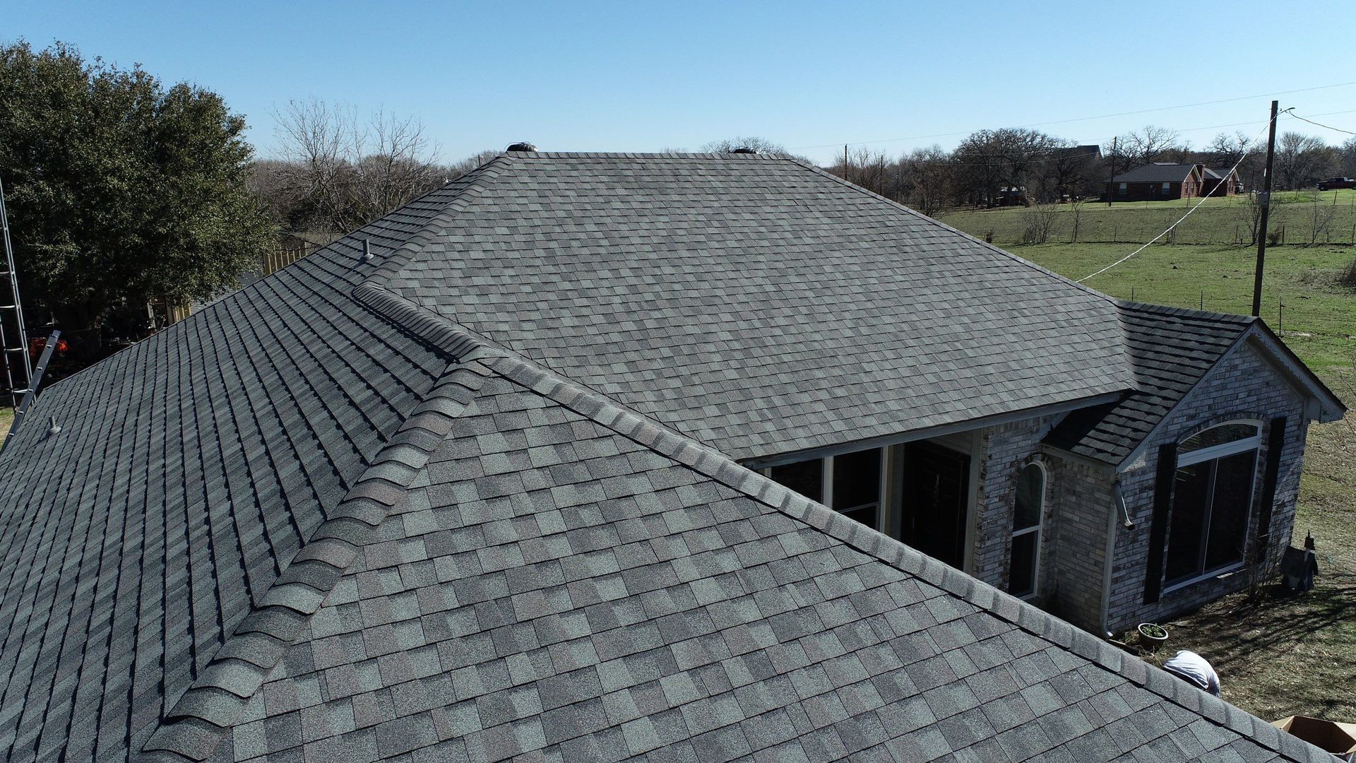 Gray shingled roof of a house, viewed from above, on a sunny day.