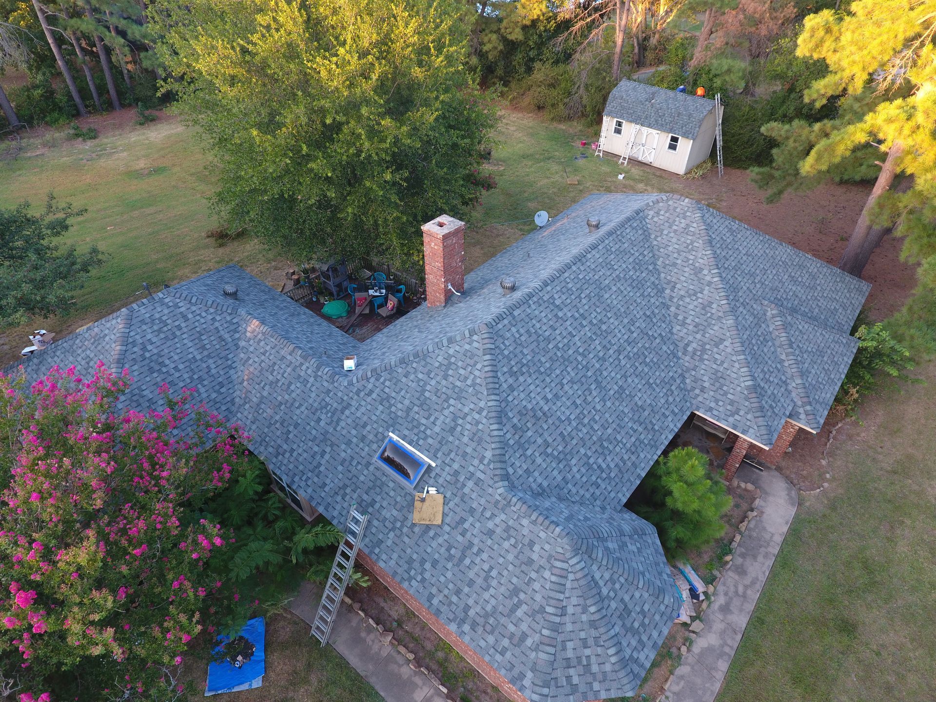 Overhead view of a house with a new blue-gray roof. A chimney and small shed are visible in the yard.