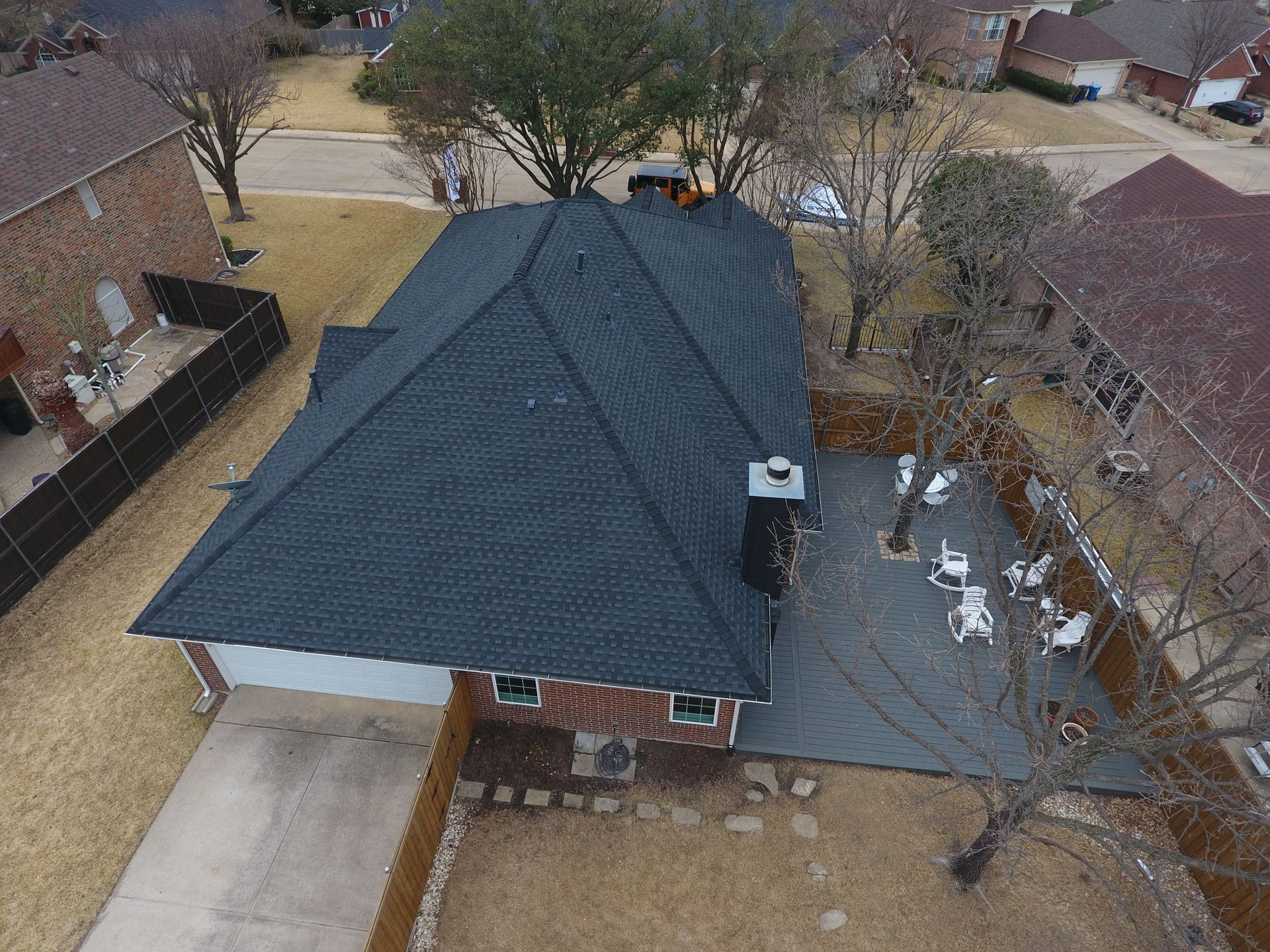 Overhead view of a home with a new black roof, a patio with chairs, and a driveway.
