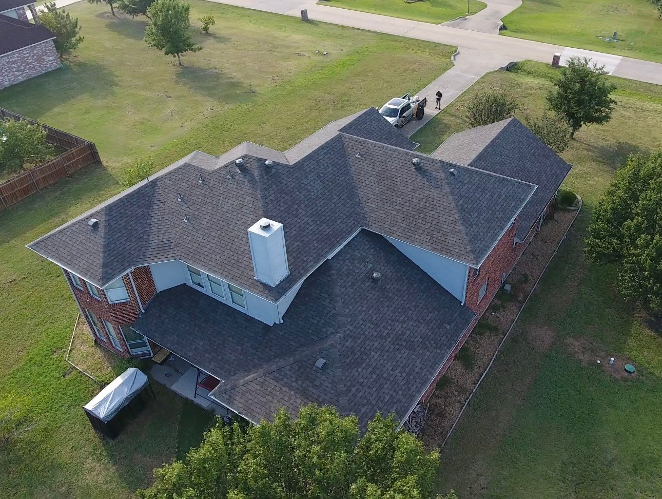 Aerial view of a two-story brick house with a dark gray shingled roof and a white chimney.