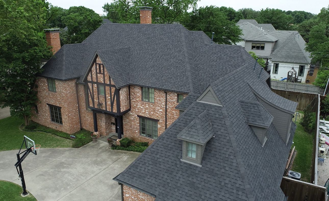 Brick Tudor home with a dark gray roof and a driveway with a basketball hoop.