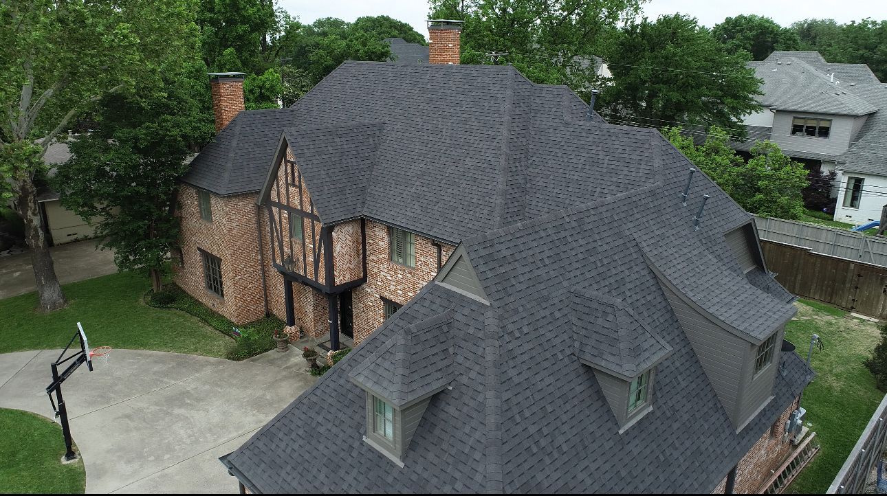 An aerial view of a large brick house with a black roof. An aerial view of a large brick house with a black roof.