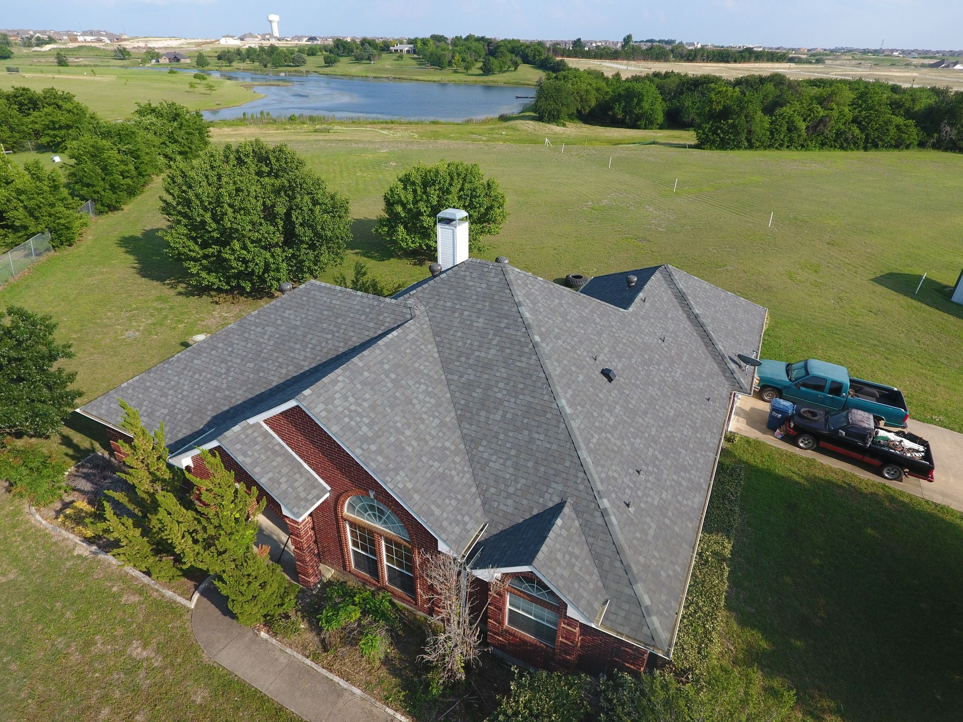 A large, red brick house with a gray roof is surrounded by a grassy yard, trees, and a lake. A large, red brick house with a gray roof is surrounded by a grassy yard, trees, and a lake.