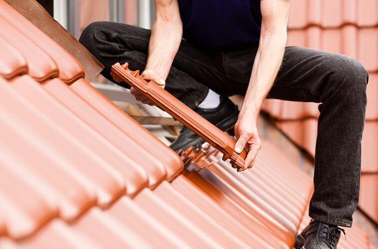 A man is sitting on top of a roof holding a piece of wood.