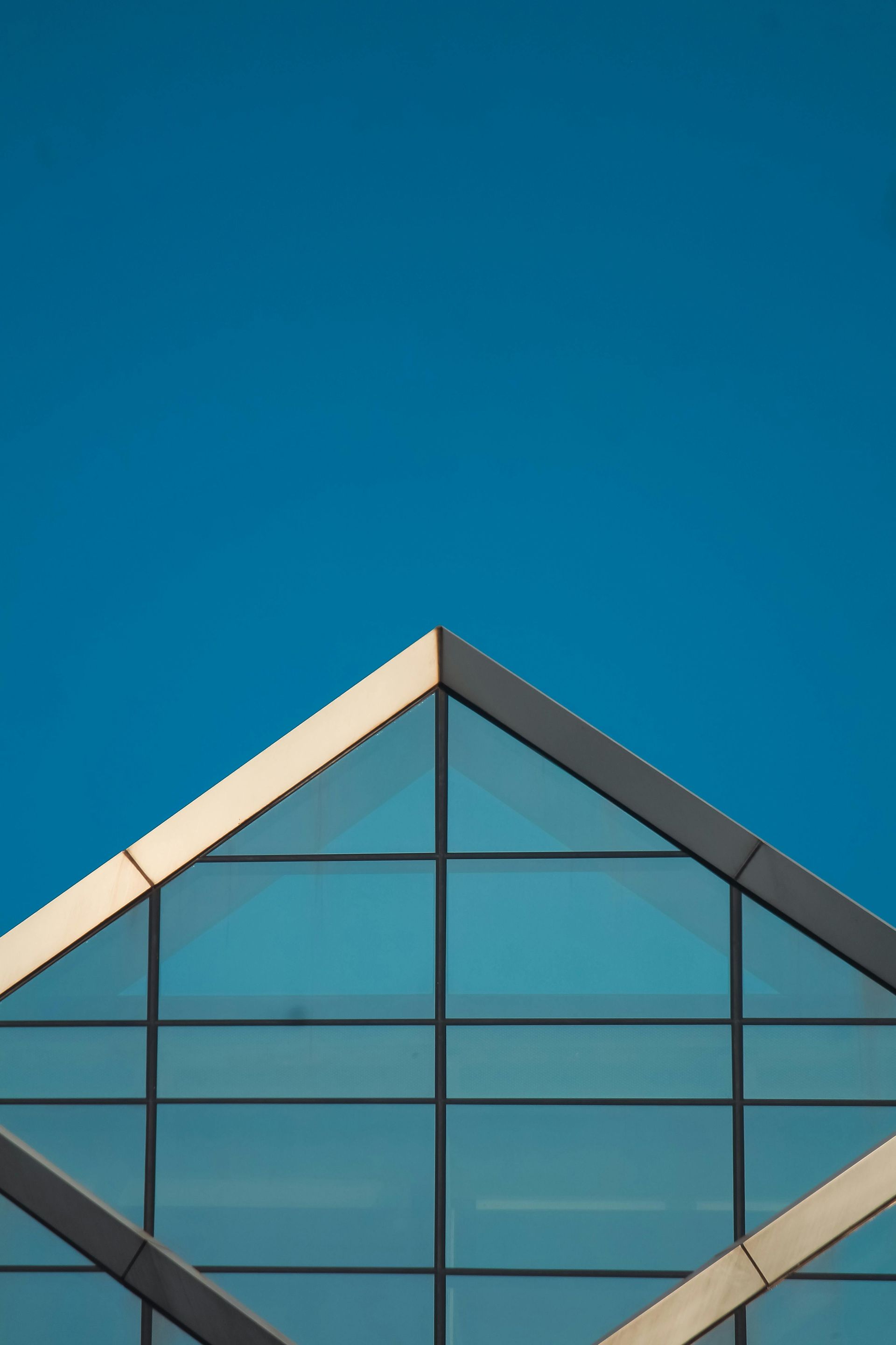 Triangular glass-paneled building roof against a bright blue sky.