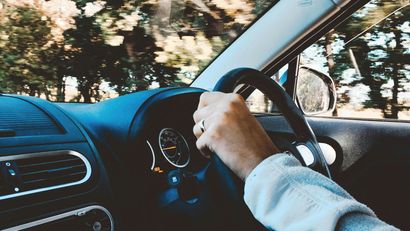 A person is driving a car with a ring on their finger.
