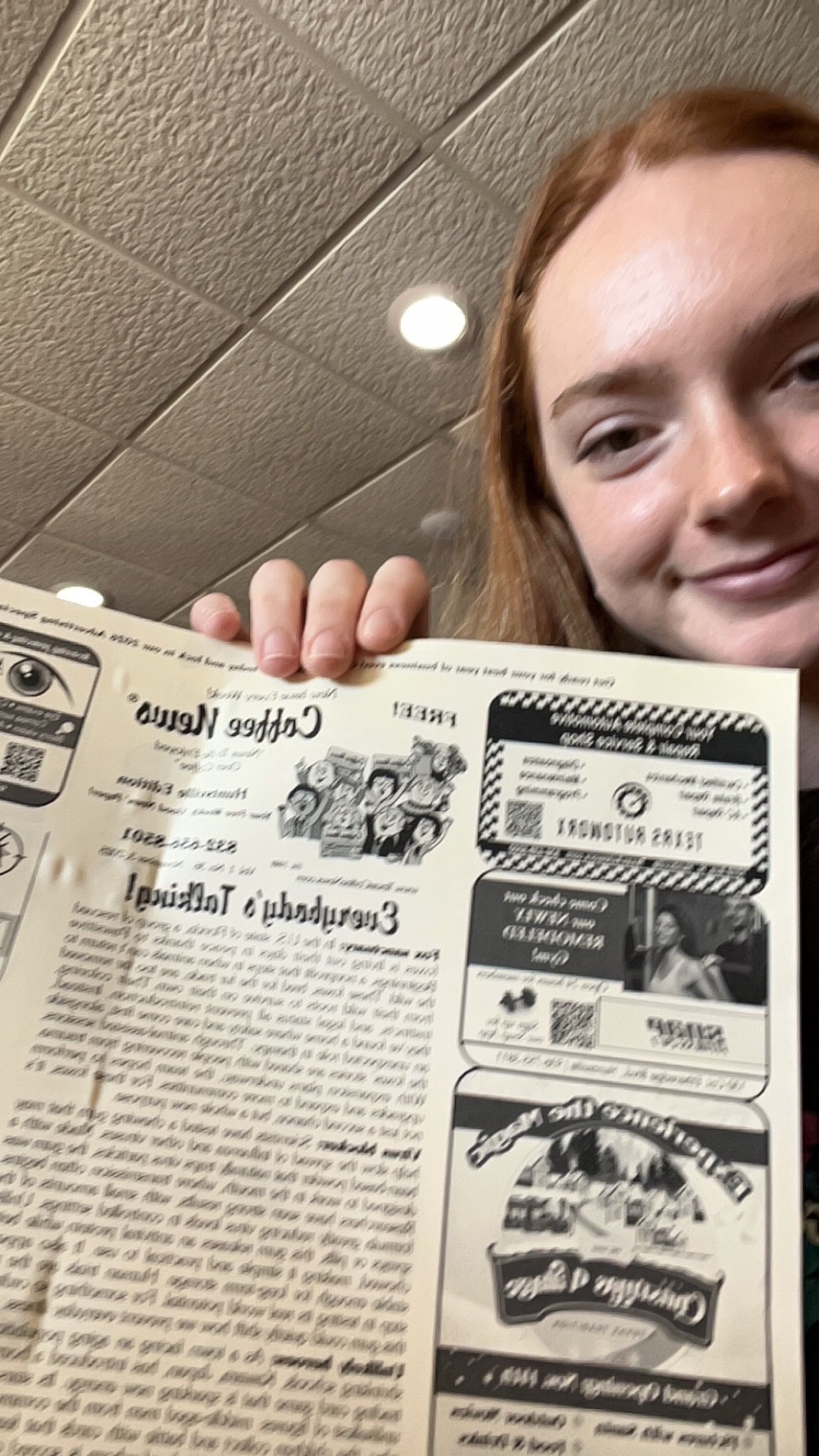 Woman holding a newspaper, smiling. The paper is titled 