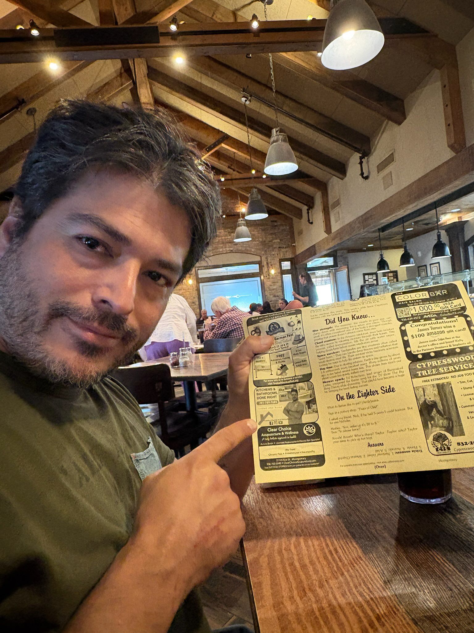 Man points to a vintage menu in a restaurant, wooden table, overhead lighting.