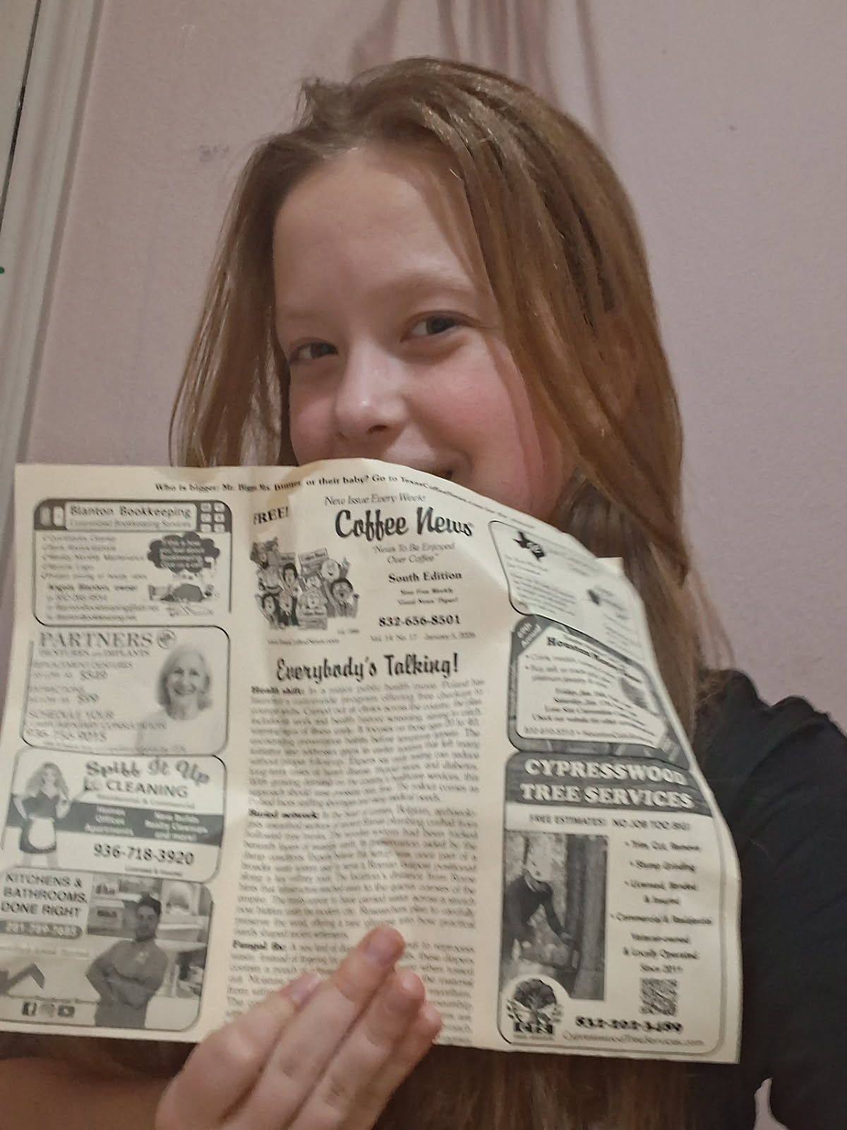 A person smiles while holding a Coffee News publication, appearing in an indoor setting.
