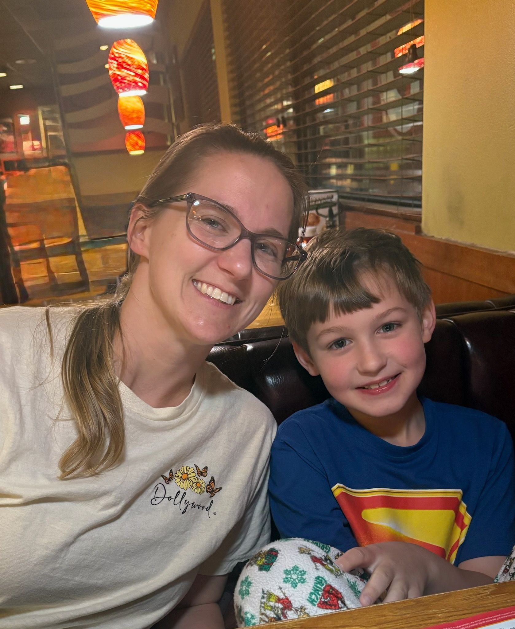 Woman with glasses and a smiling child seated at a restaurant table. They are both looking at the camera.